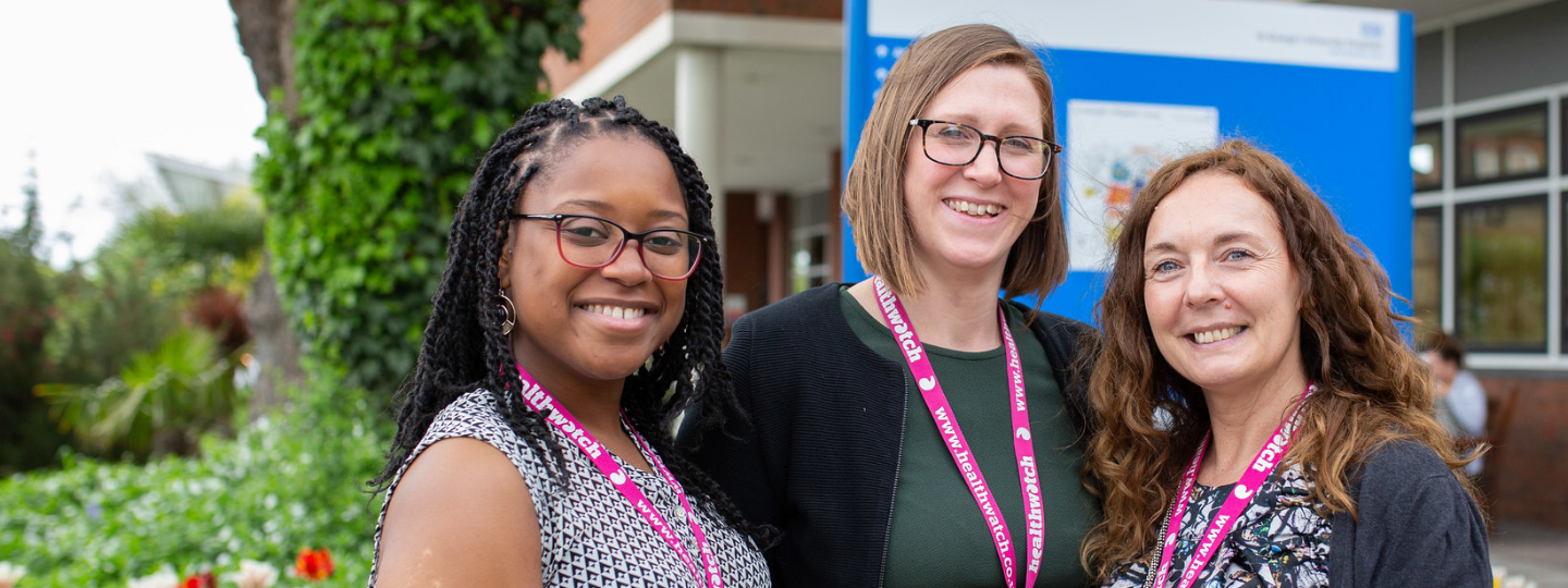 Three female staff members standing together outside a hospital entrance